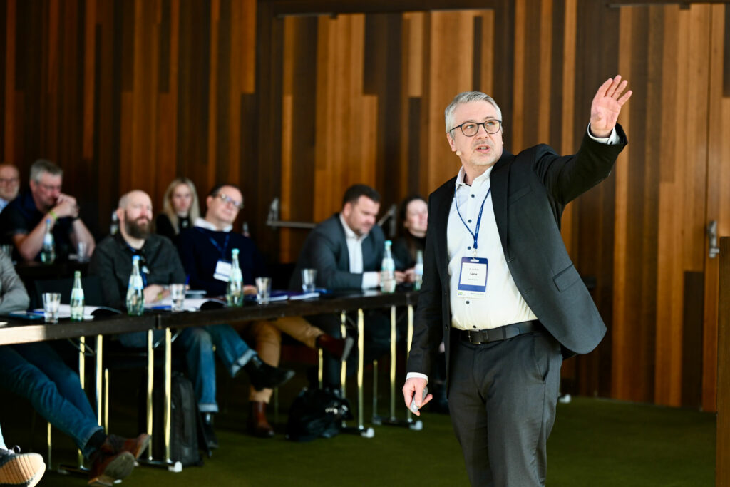 Mann mit Brille spricht vor Publikum in einem Konferenzraum